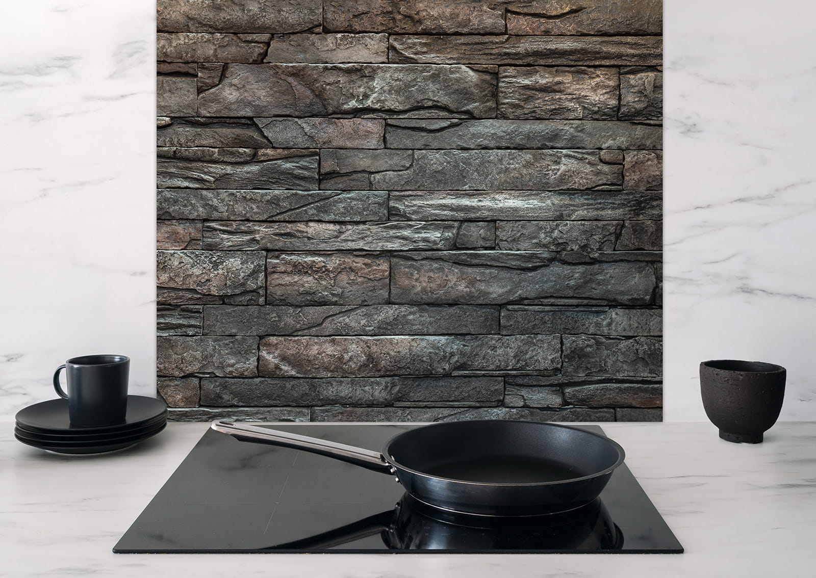 Spritzschutz "Steinwand" von ENTDECKER, zeigt eine Steintextur im Hintergrund mit einer Pfanne auf einem schwarzen Kochfeld.