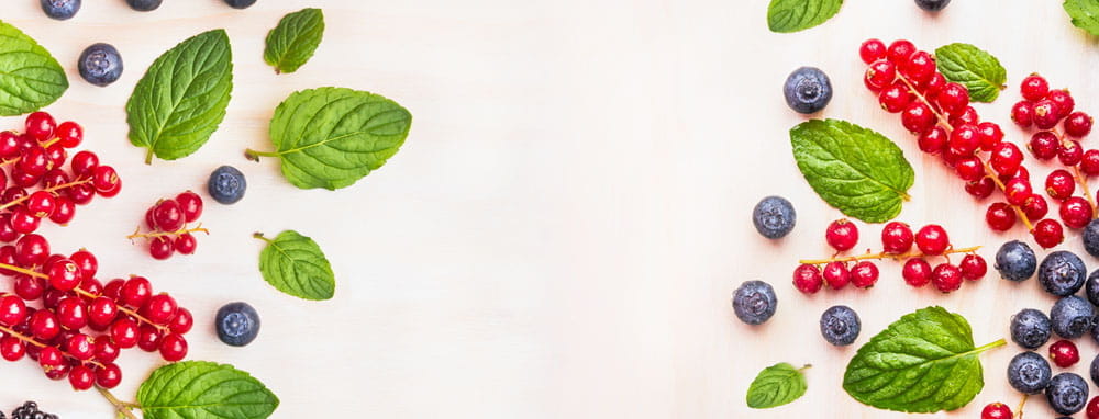 Frische rote und schwarze Beeren sowie Minzblätter auf einem hellen Hintergrund.