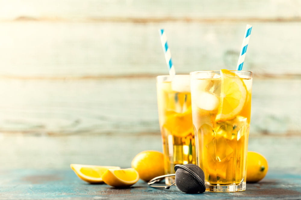 Zwei Gläser mit Orangenlimonade, dekoriert mit Zitronenscheiben und blauen Strohhalmen, auf einem Holztisch.